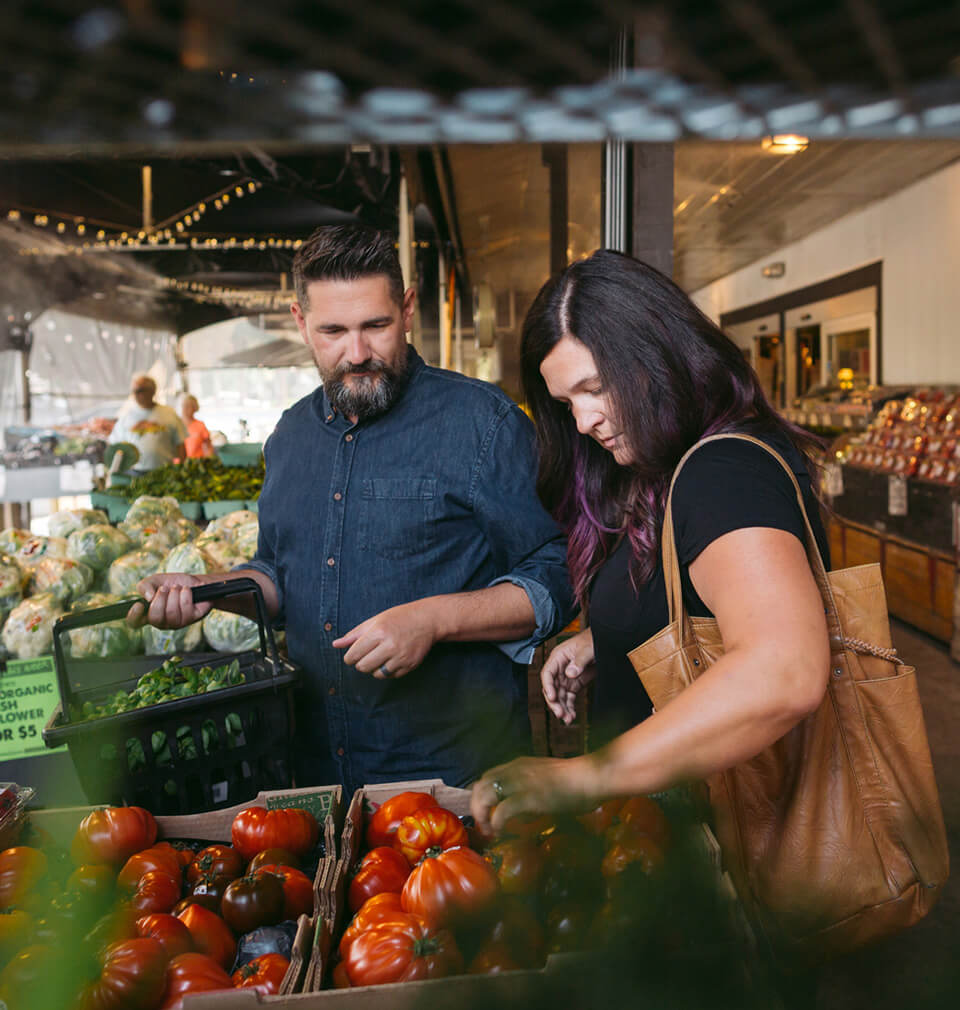 a man and a woman shop for vegetables at a store