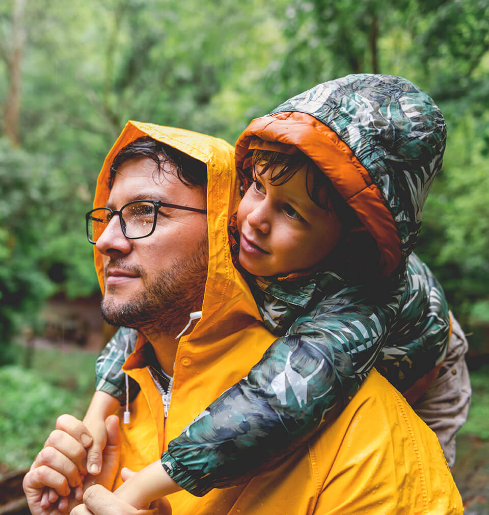 a man in a raincoat holds his kid on his shoulders