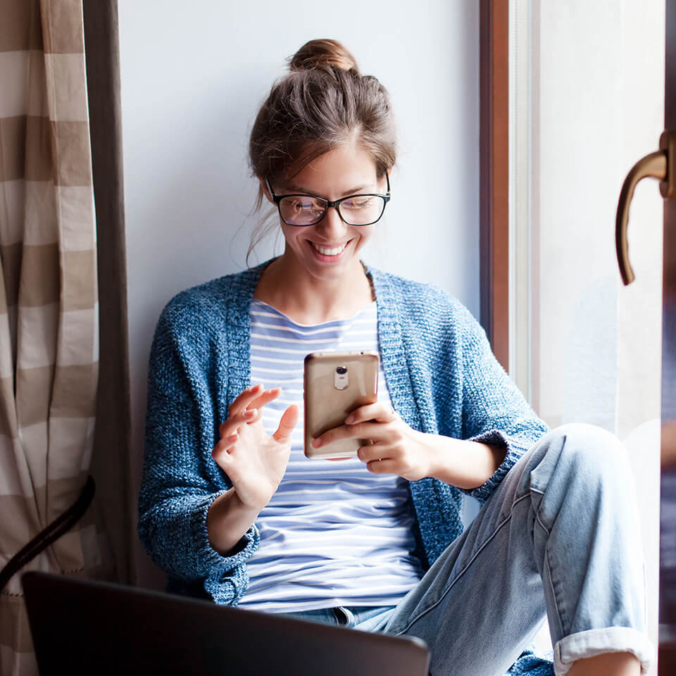 a woman smiles at her phone while sitting in the corner