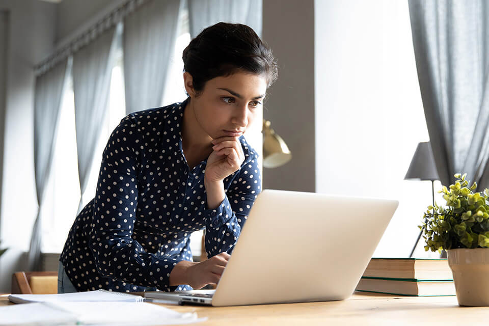 a woman in a blue polka dot blouse hunches over a laptop