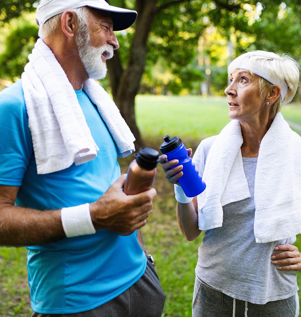 older couple in running outfits talk while holding water bottles