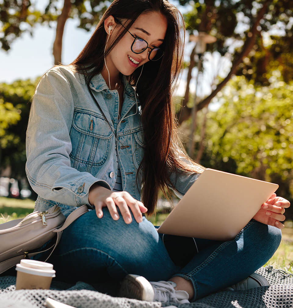 a woman listens to headphones while on her laptop outside