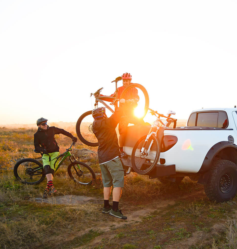 three guys outdoors with their bikes and a white truck
