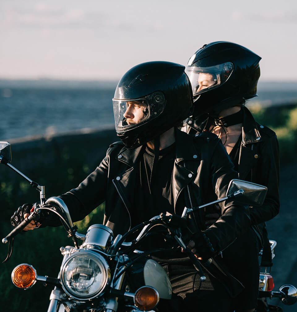 man and woman in motorcycle helmets look out over the ocean