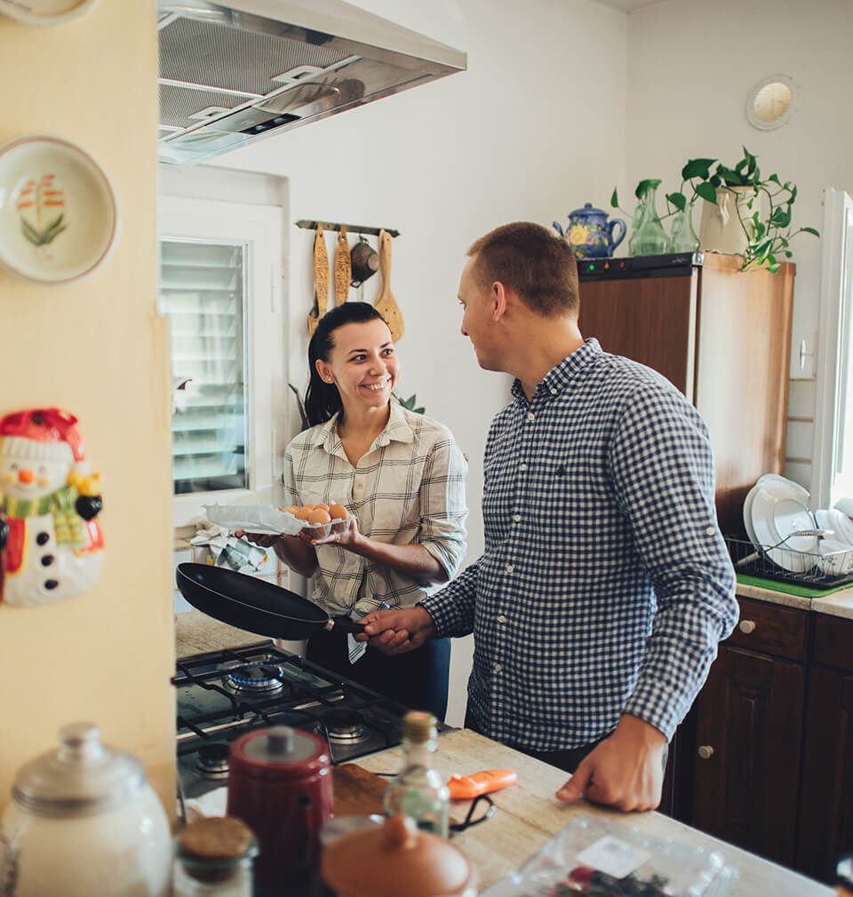 a woman smiles at a man who is cooking eggs