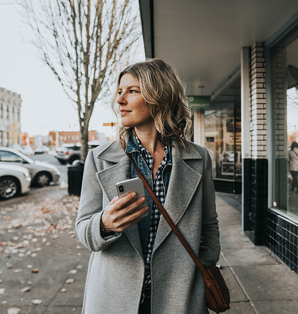 a woman in a gray coat looks to the side while holding a phone